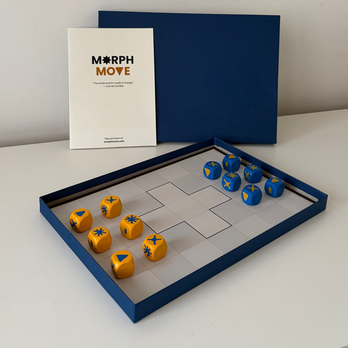 MorphMove tabletop game with board, blue and yellow marked dice, rulebook, and navy box